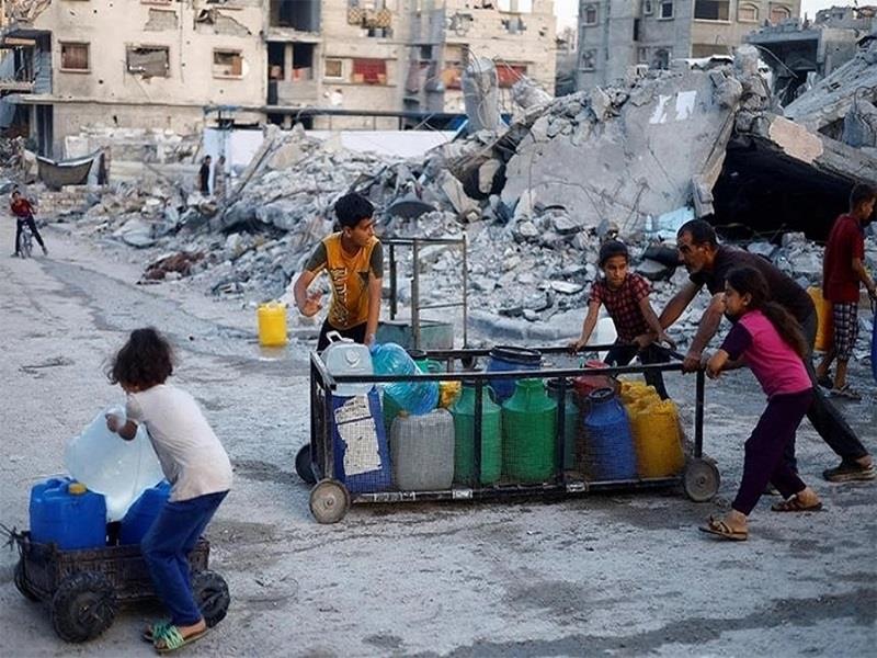 Một người đàn ông Palestine và trẻ em đẩy xe chở các thùng chứa nước ở Gaza. (Ảnh: Reuters)