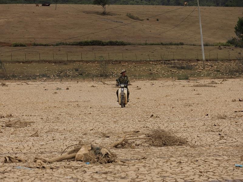 Một nông dân chạy xe gắn máy giữa lòng hồ khô cạn